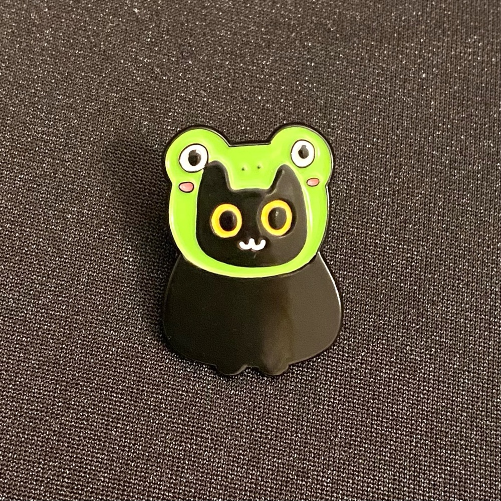 Happy kitty shows off her fun frog hat | Enamel pins or magnets are 3 for $18